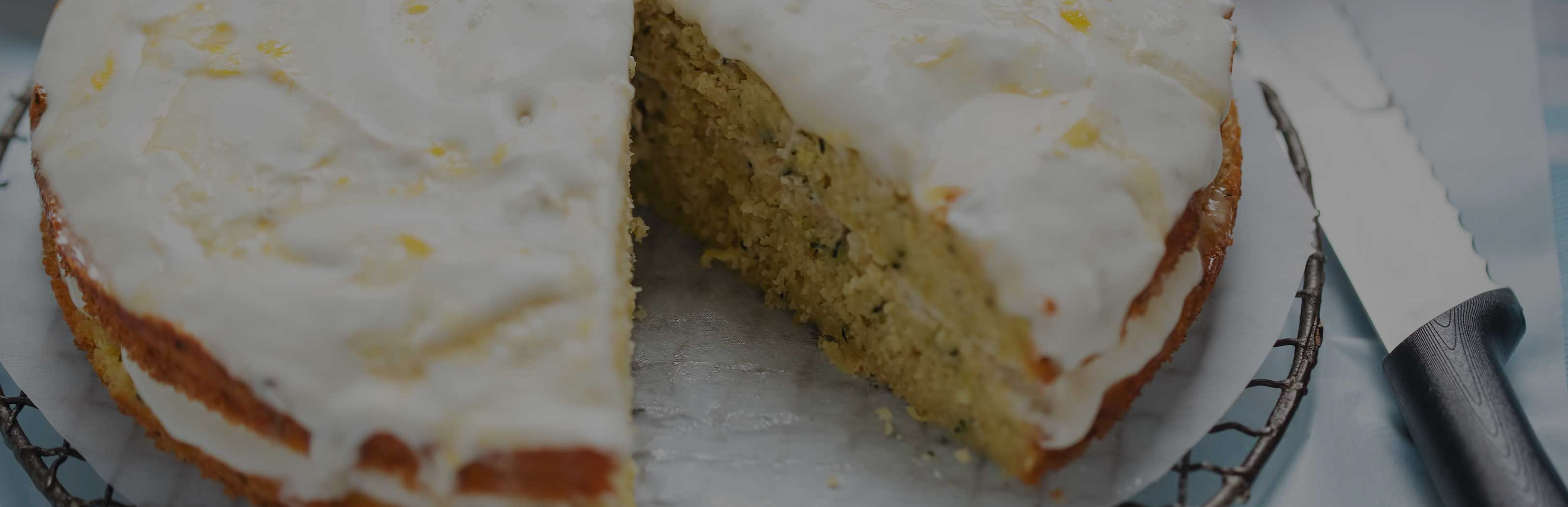 Close-up of sliced iced lemon protein cake showing moist crumb and white lemon glaze on a cooling rack with a knife