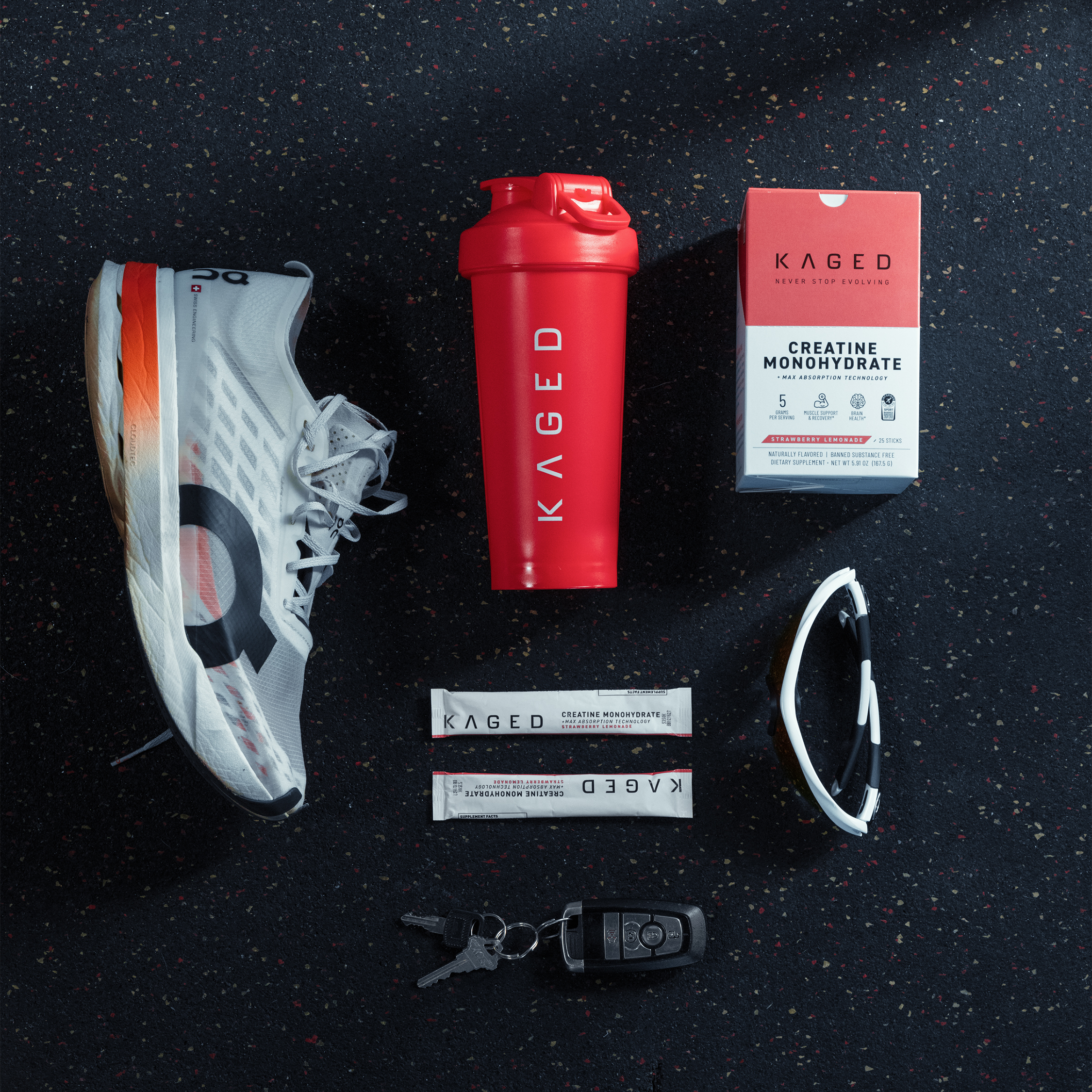 Top down view of 28oz Crimson KAGED shaker bottle with flip lid on speckled gym floor with running shoe and creatine box