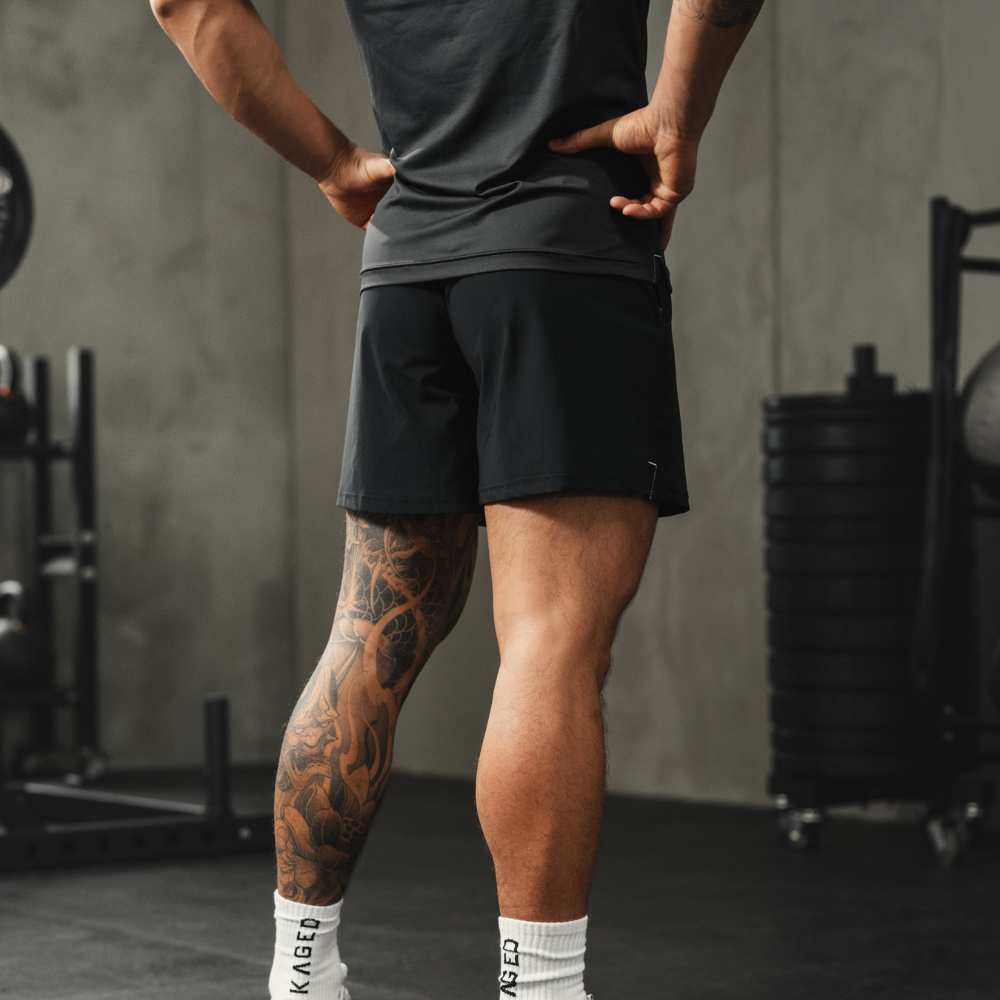 Rear view of Ascent Performance Shorts on model, athletic fit in black showing short inseam and breathable fabric in gym setting