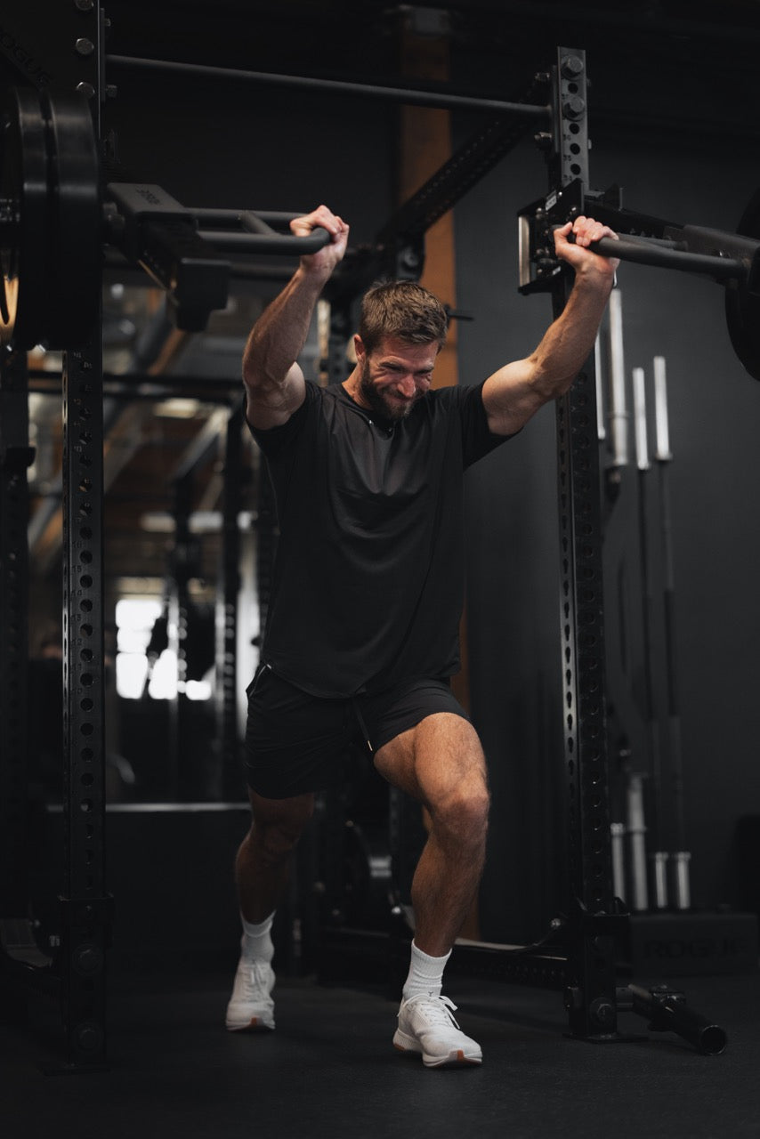 Athletic man performing an overhead lunge holding a bar in a gym during strength training