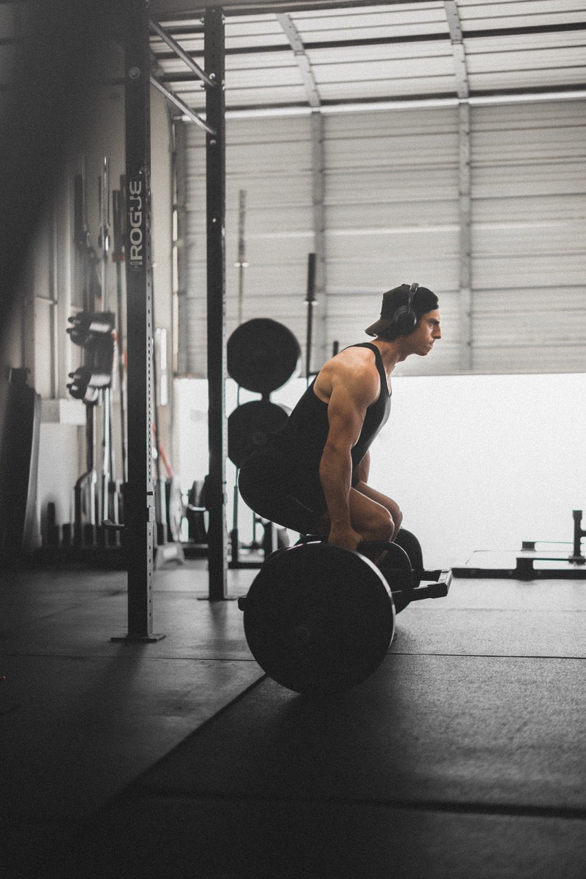 Athlete deadlifting a barbell in a bright industrial gym, wearing headphones and a black tank top
