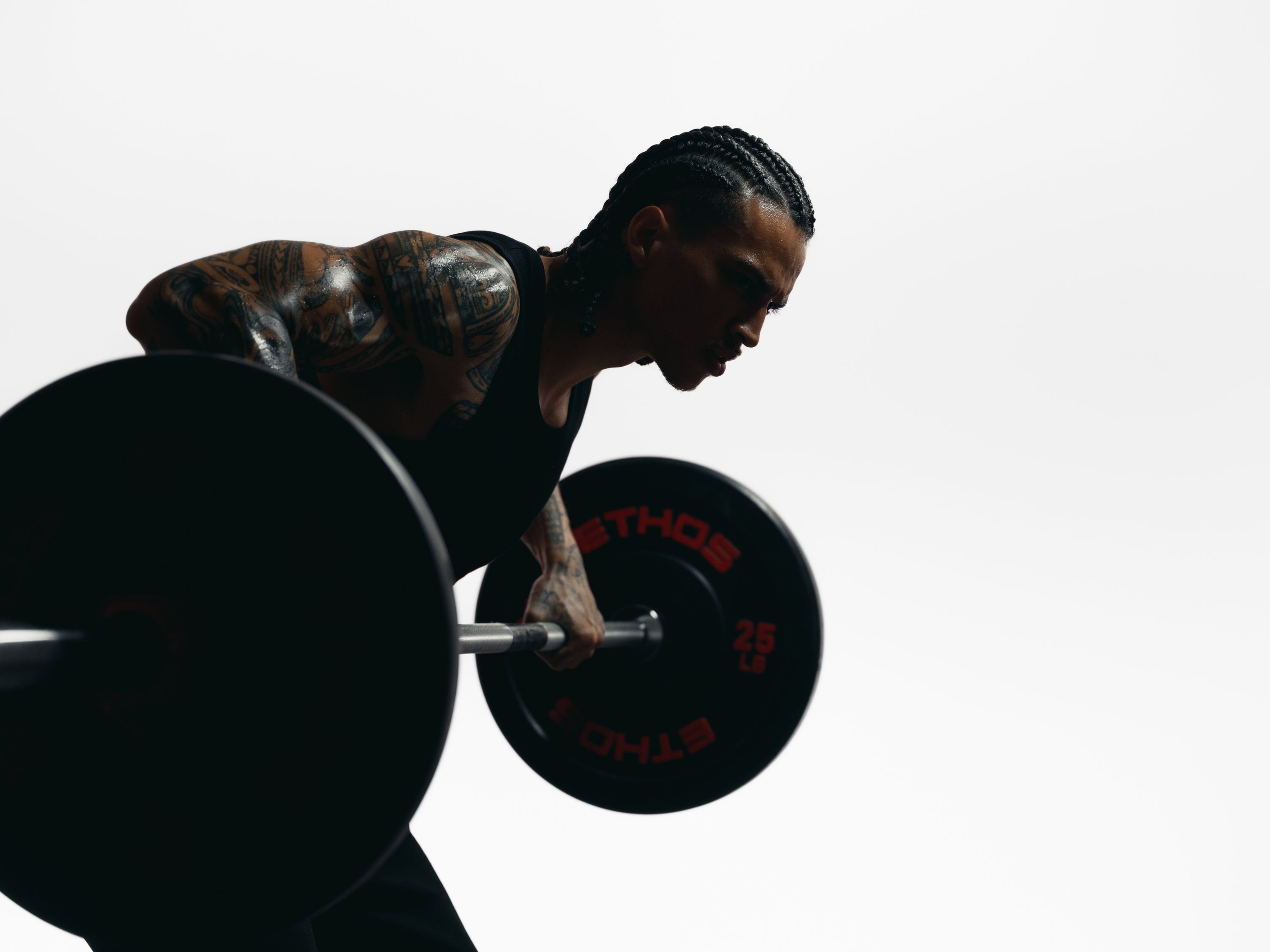 Athlete performing a bent-over barbell row in a high-contrast studio, focused expression and tattooed arm visible