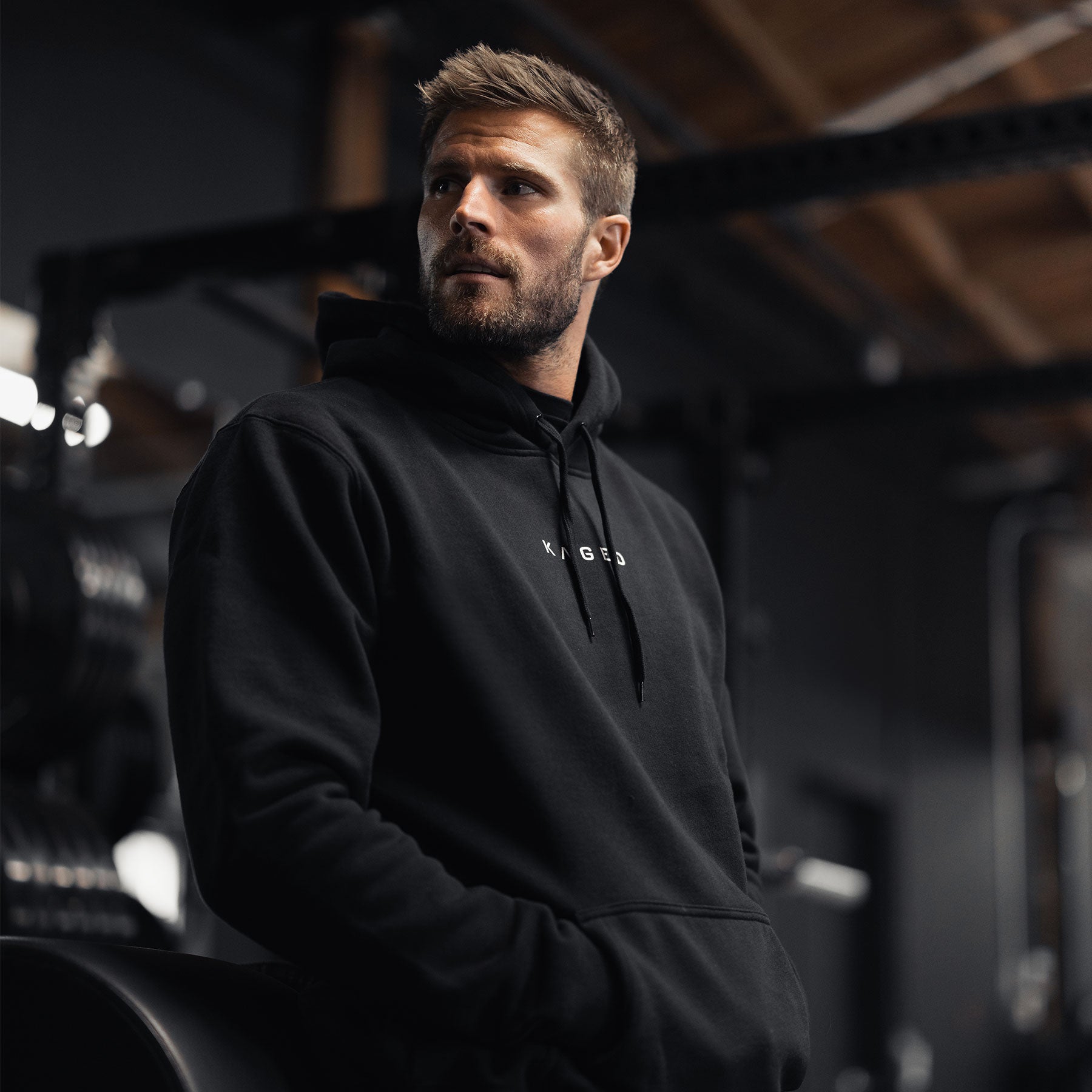 3/4 view of Never Stop Evolving hoodie in black showcasing KAGED logo, hood and kangaroo pocket, worn by model in gym #color_black