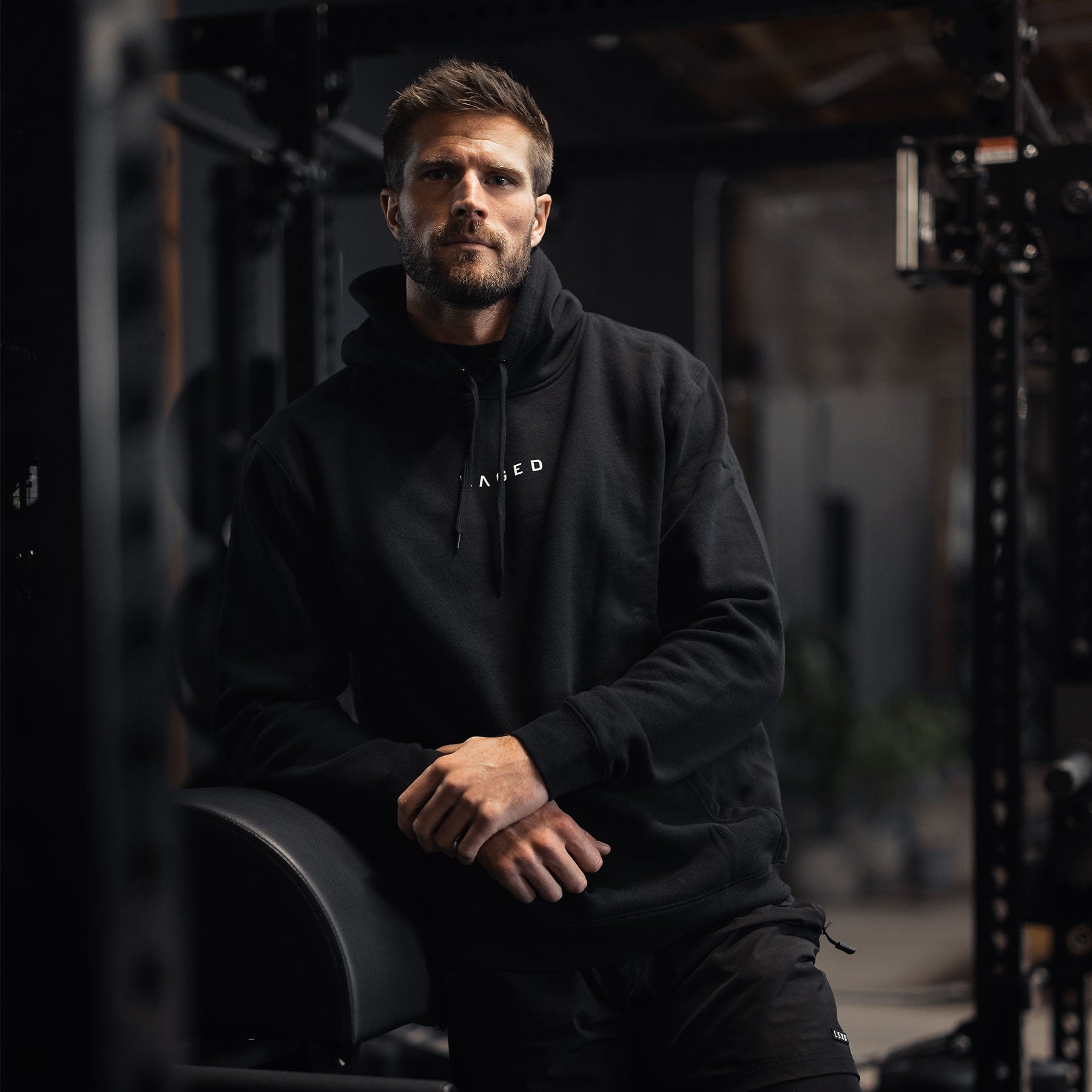 Three-quarter front view of Never Stop Evolving hoodie in black on male model showing pullover hood, kangaroo pocket, and small chest logo in gym setting #color_black
