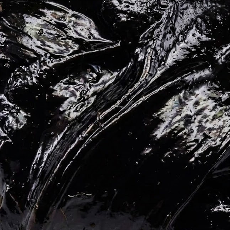 Close-up of PrimaVie purified shilajit resin showing glossy dark, tar-like texture on black background