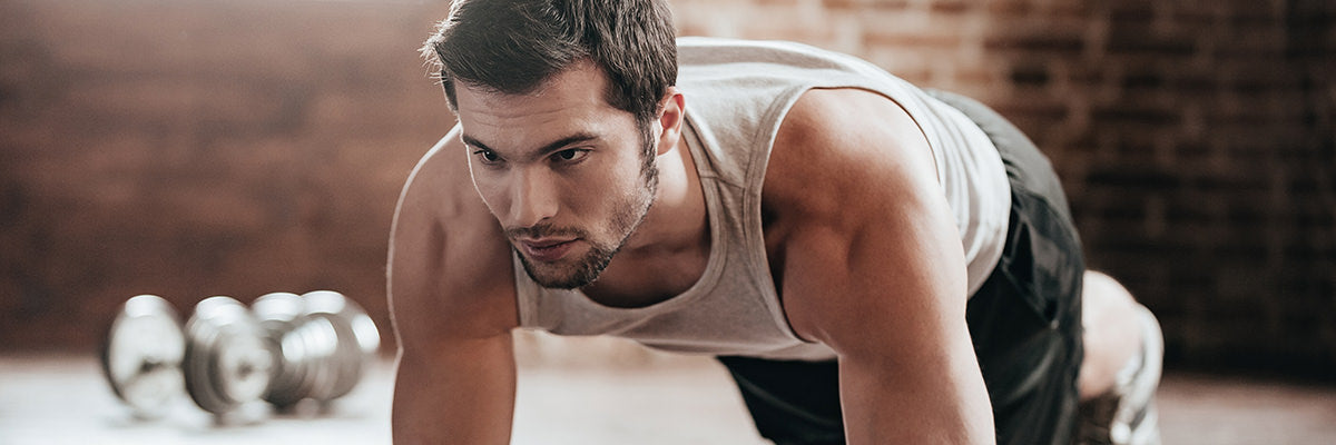 Athletic man holding a forearm plank in a gym with a brick wall and dumbbells in the background
