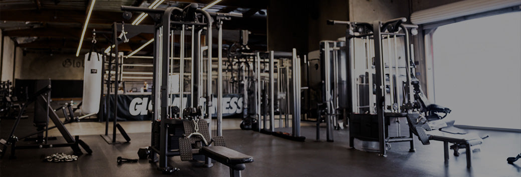 Empty gym with cable machines, benches, and a hanging heavy bag lit by natural light from a large window