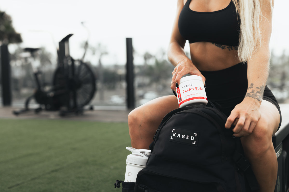 Woman placing KAGED Clean Burn supplement tub into a KAGED backpack at an outdoor gym
