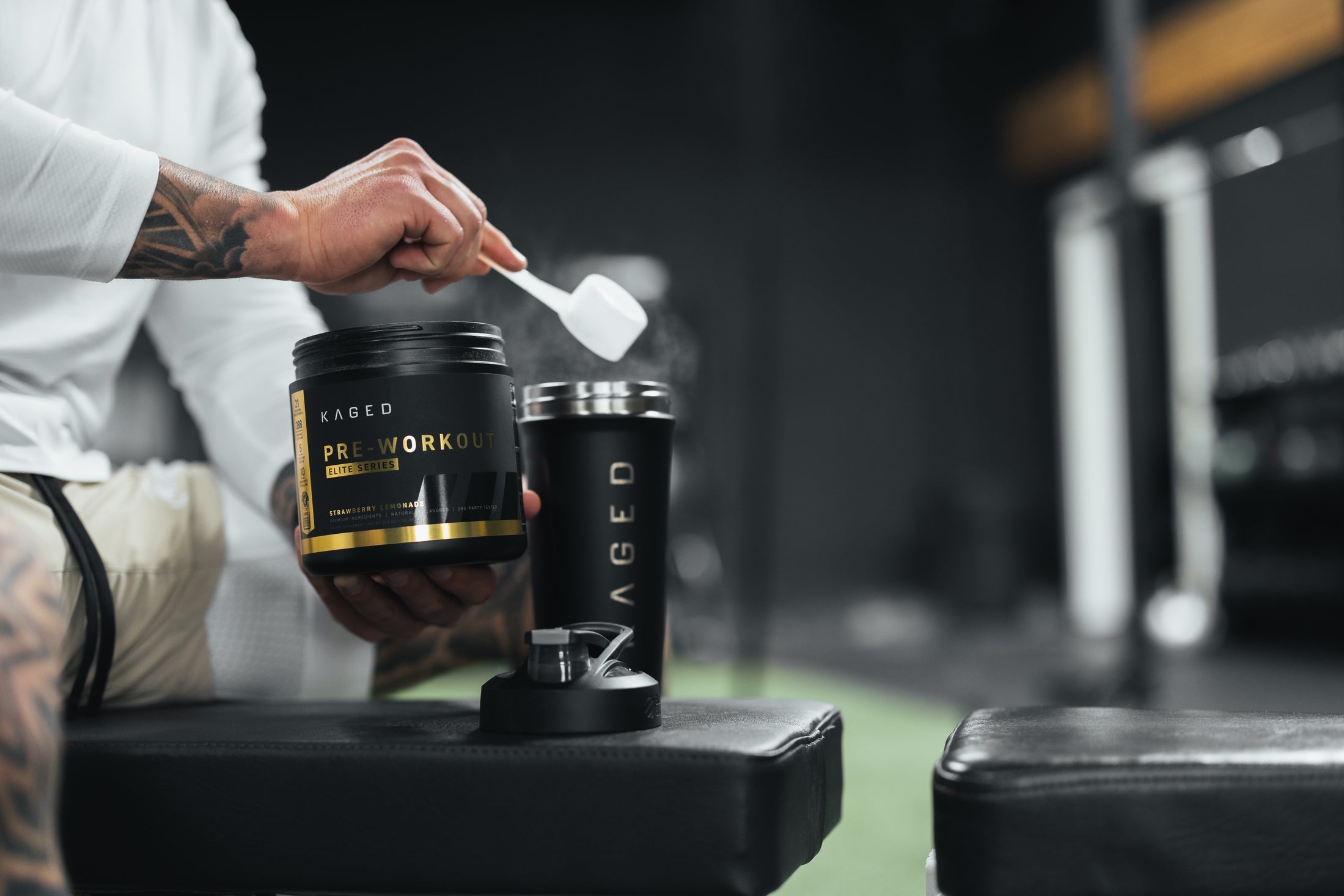 Person scooping KAGED Pre-Workout powder from a tub into a KAGED shaker in a gym