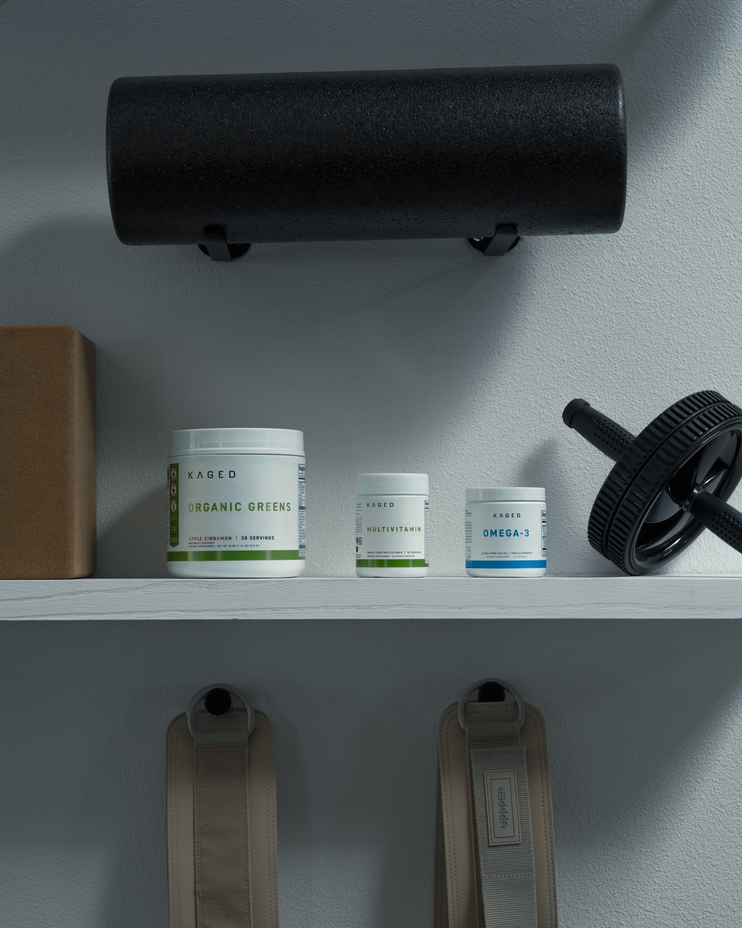 Front shelf view of KAGED Omega-3 supplement jar alongside multivitamin and Organic Greens tubs on a home gym shelf