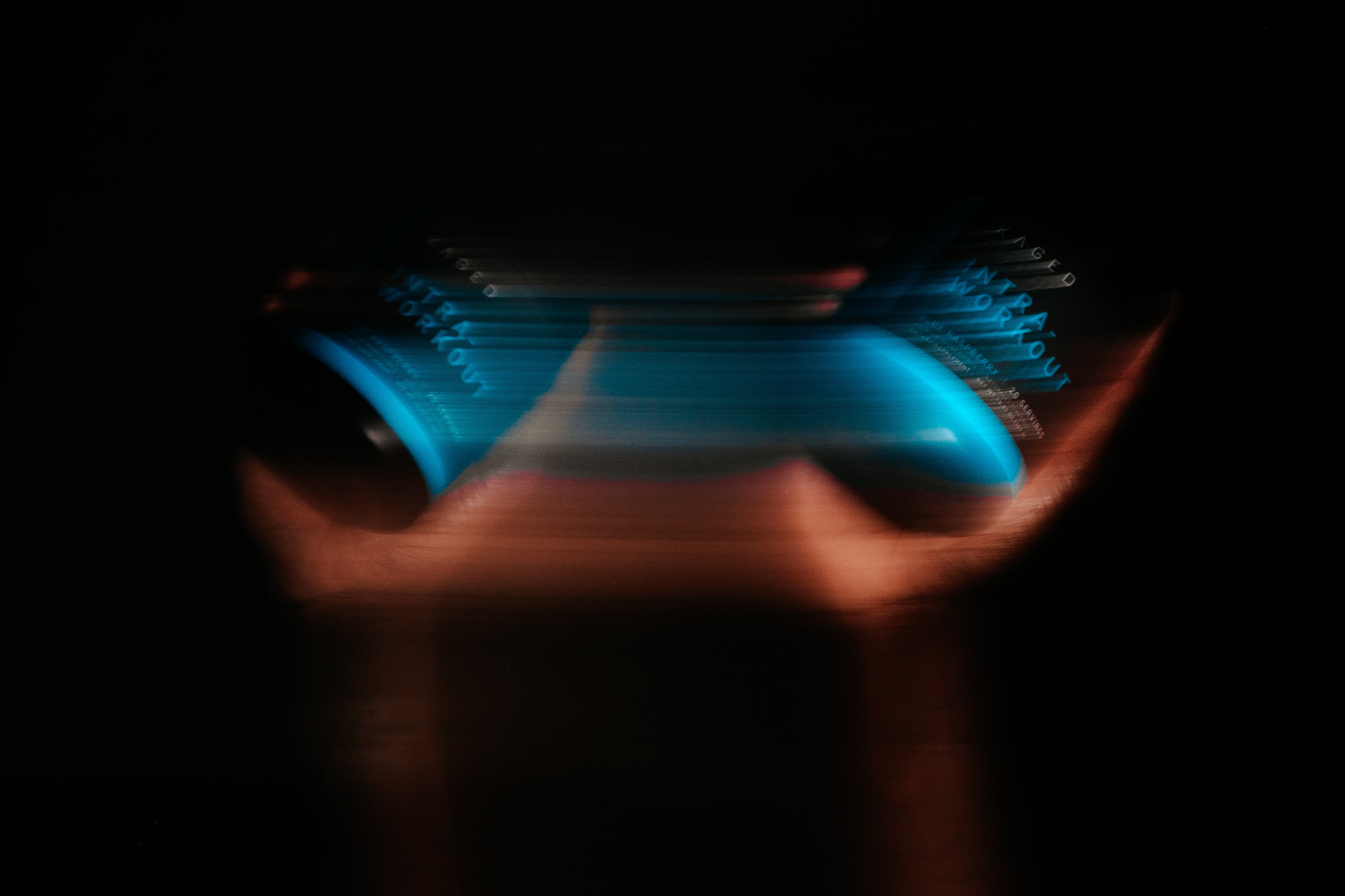 Blurred motion shot of a blue KAGED supplement tub label with streaked cyan and orange light