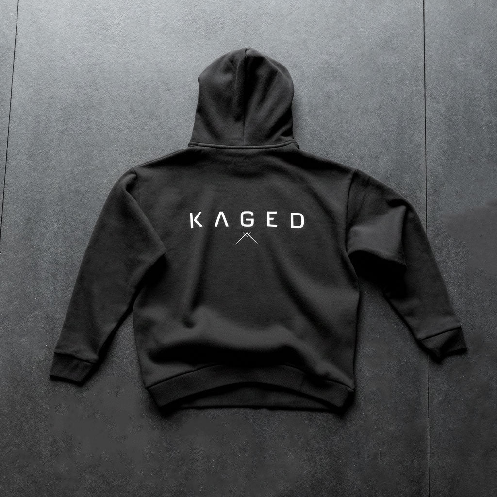 Back view of Ascent Hoodie showcasing white KAGED logo on black fabric on dark textured background