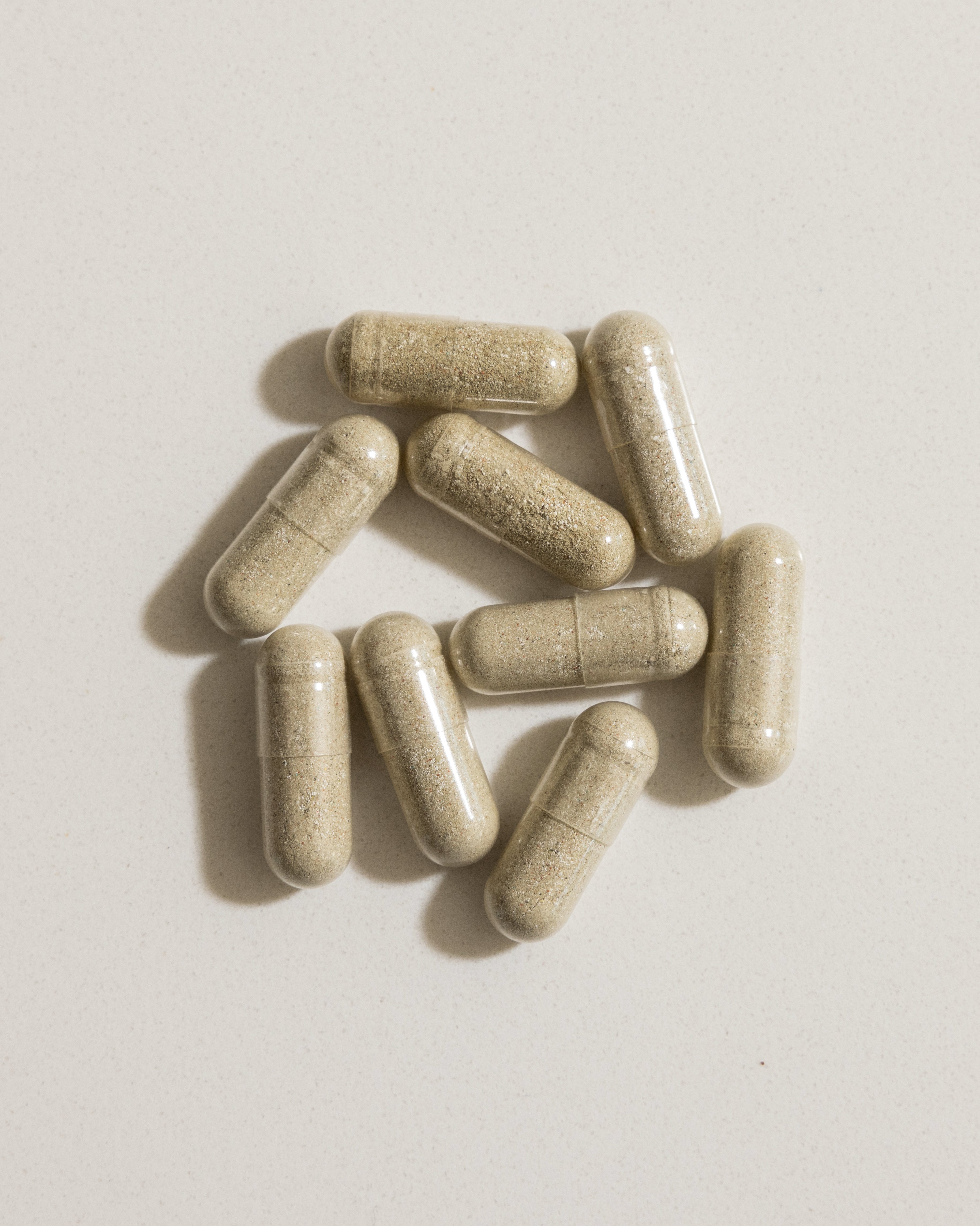 Top-down view of Kaged multivitamin capsules with transparent shells revealing beige whole-food powder on a light background