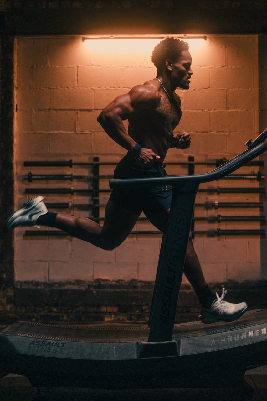 Athletic man running on a curved treadmill in a dimly lit gym, mid-stride during a cardio workout