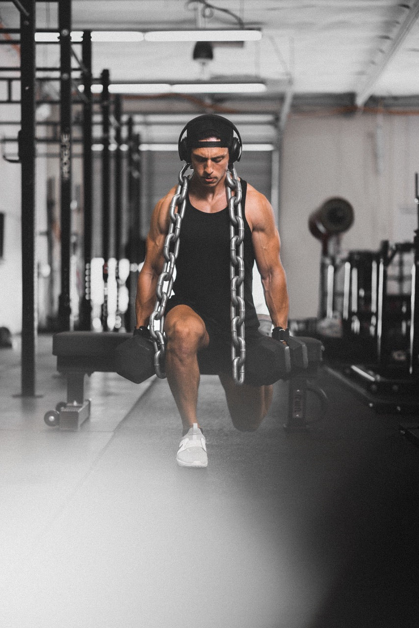 Athlete performing a weighted walking lunge with heavy chains and dumbbells in a gym