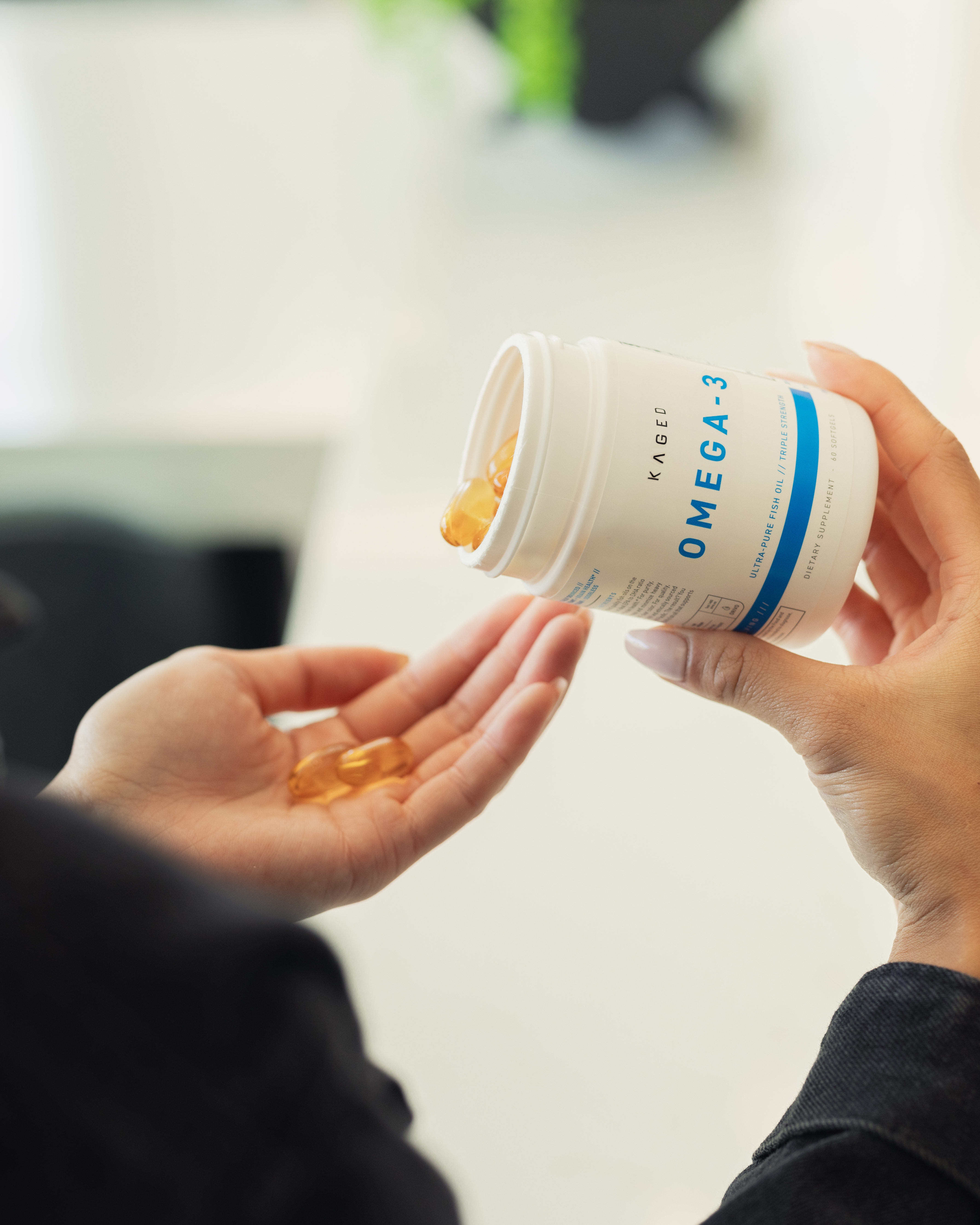 Person pouring amber omega-3 softgels from a white Kaged bottle into another person's open palm