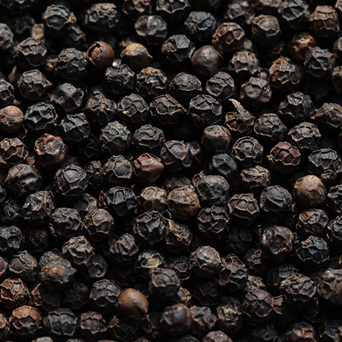 Close-up of whole black peppercorns representing Bioperine black pepper extract, showing coarse texture on a dark background