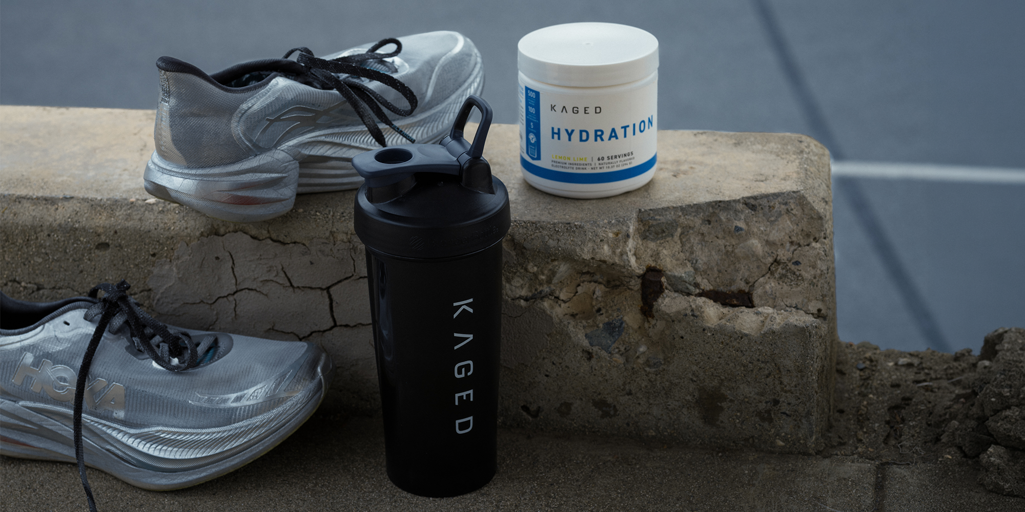 Front view of black BlenderBottle Classic 28 oz showing SpoutGuard lid and KAGED logo with running shoes on concrete