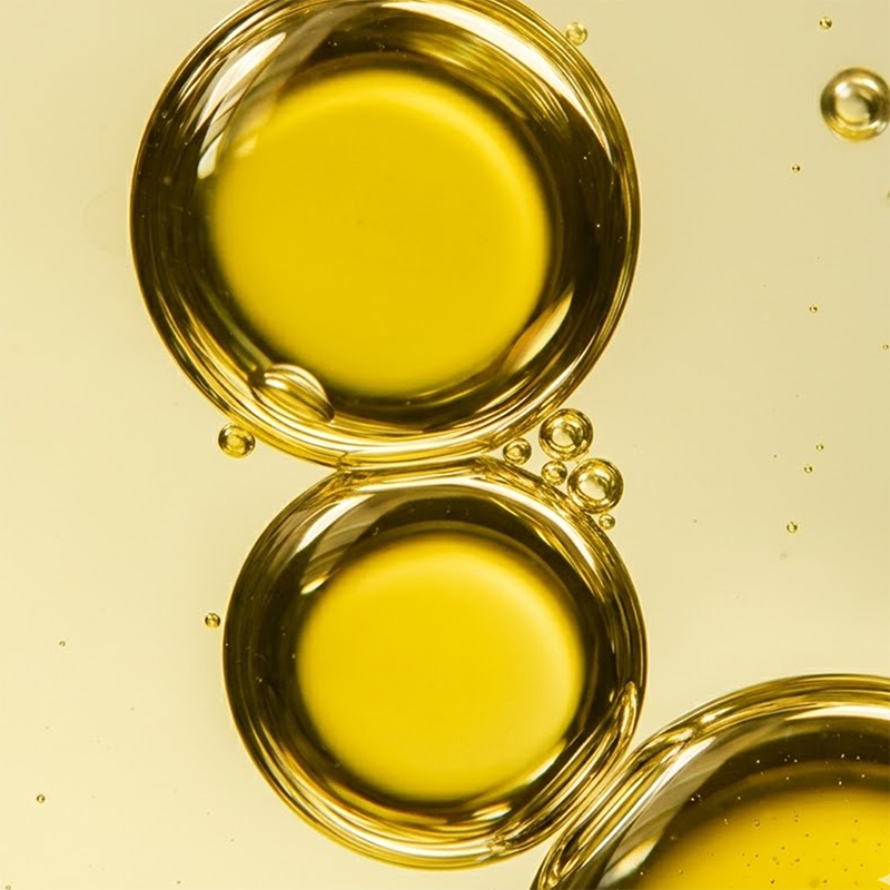 Close-up of coconut oil droplets showcasing smooth golden texture with pale yellow background