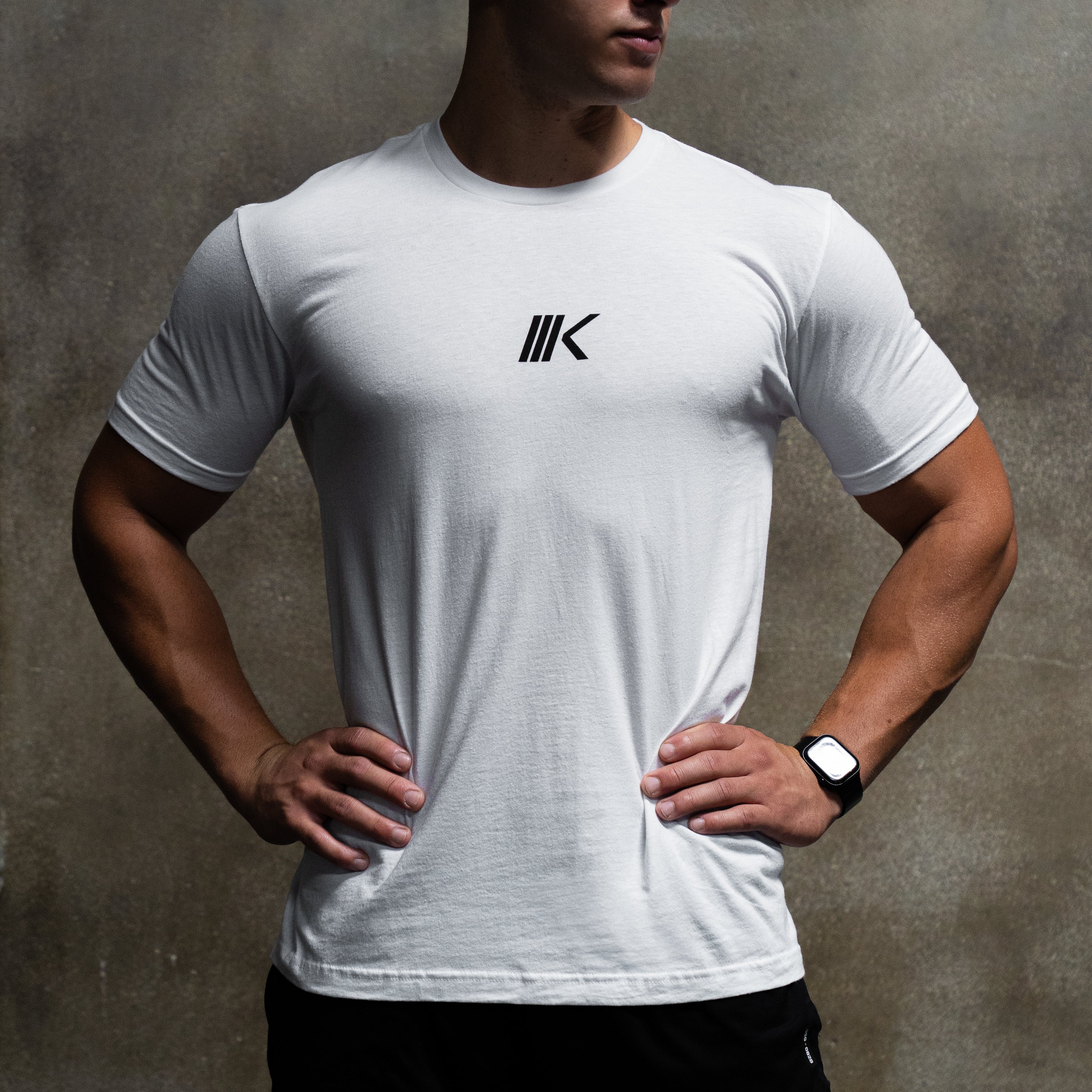 Front view of Slant Tee in white on model, showing centered black slant logo on chest with gray textured background #color_white
