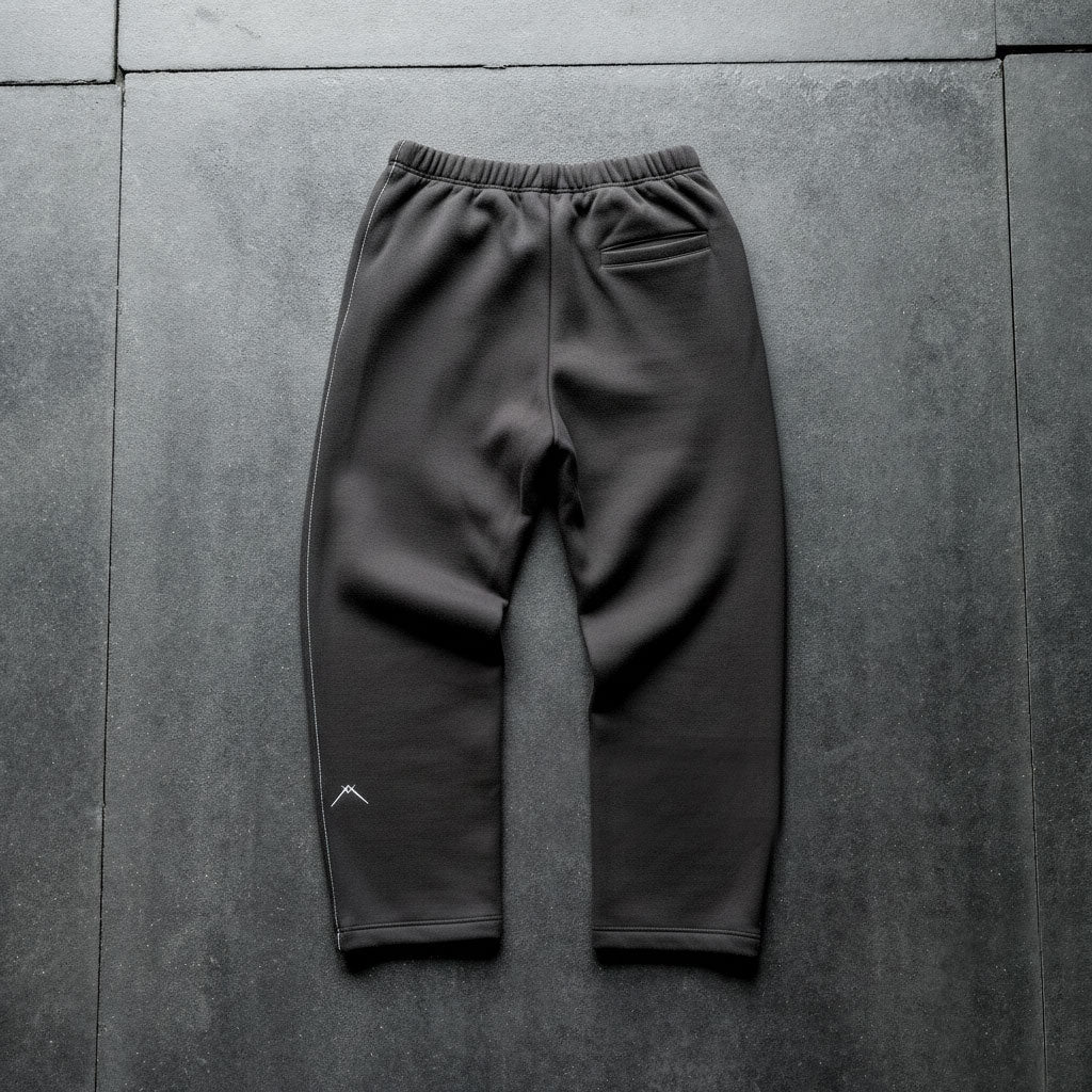 Back view of Ascent straight-leg sweats with back zip pocket, white side-seam stitch, and Ascent symbol on dark floor