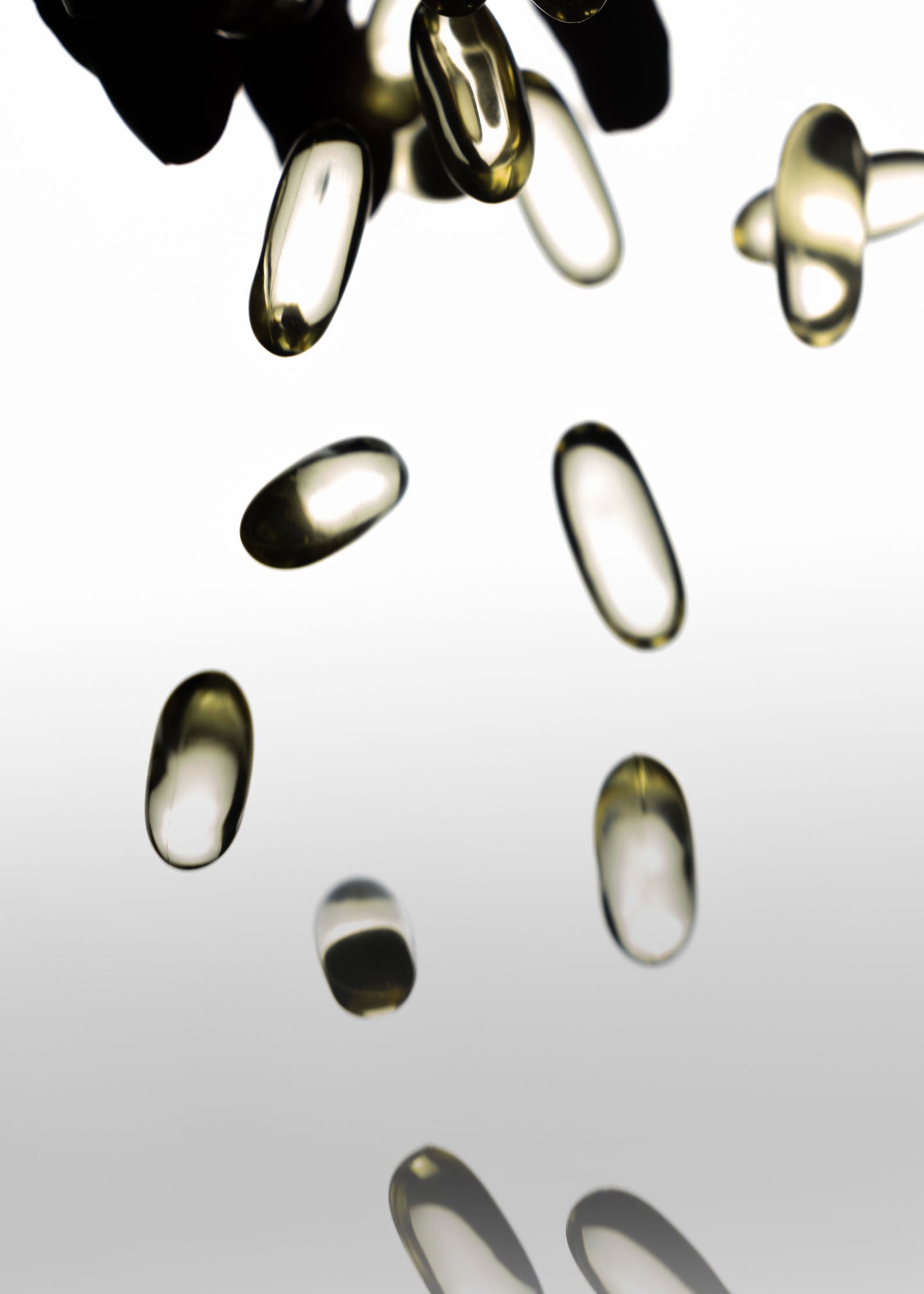 Close-up of supplement softgel capsules falling, showcasing smooth glossy texture on a white background