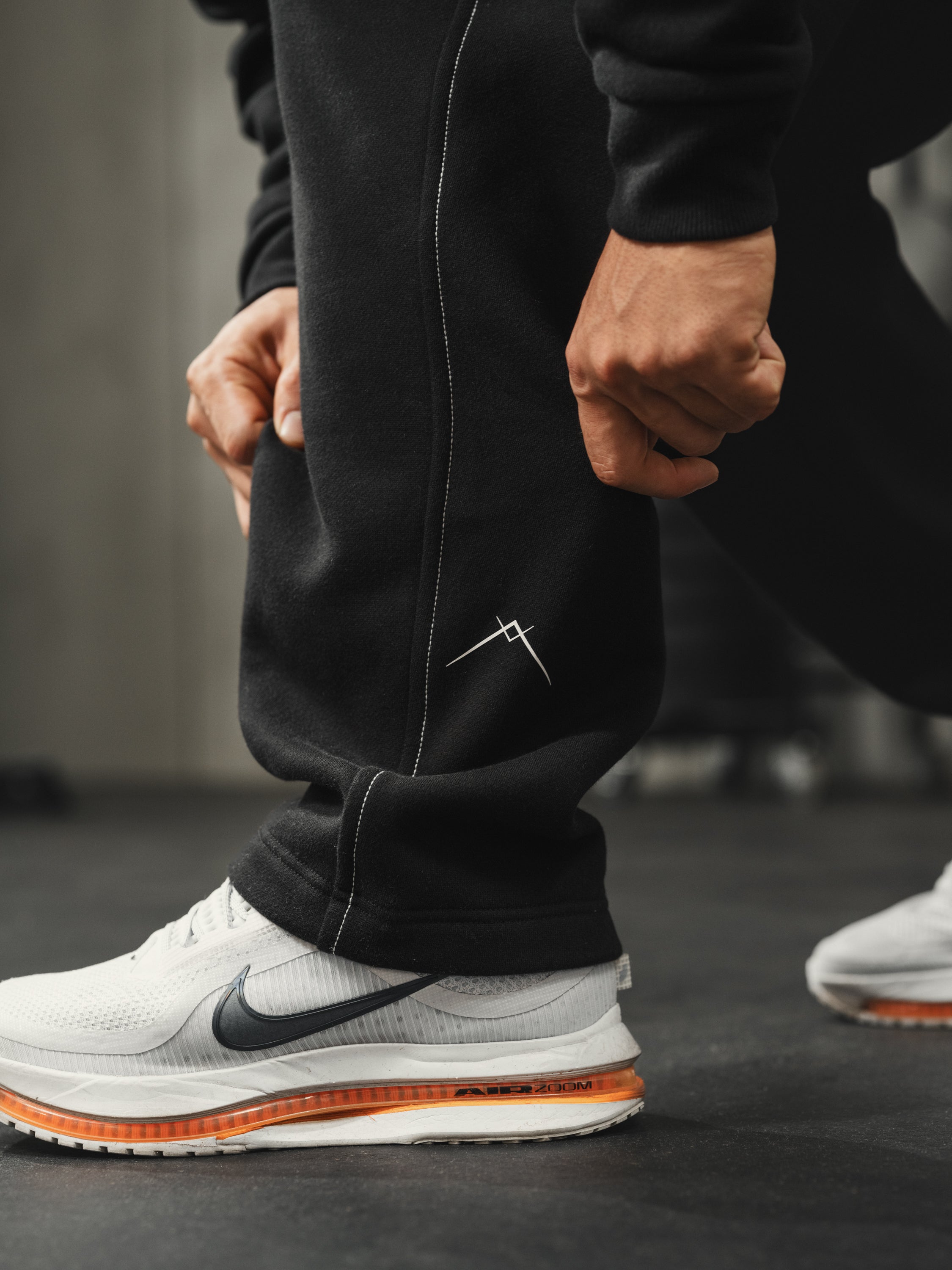 Close-up of Ascent straight-leg sweatpants showcasing white side-seam stitching and Ascent symbol against gym floor
