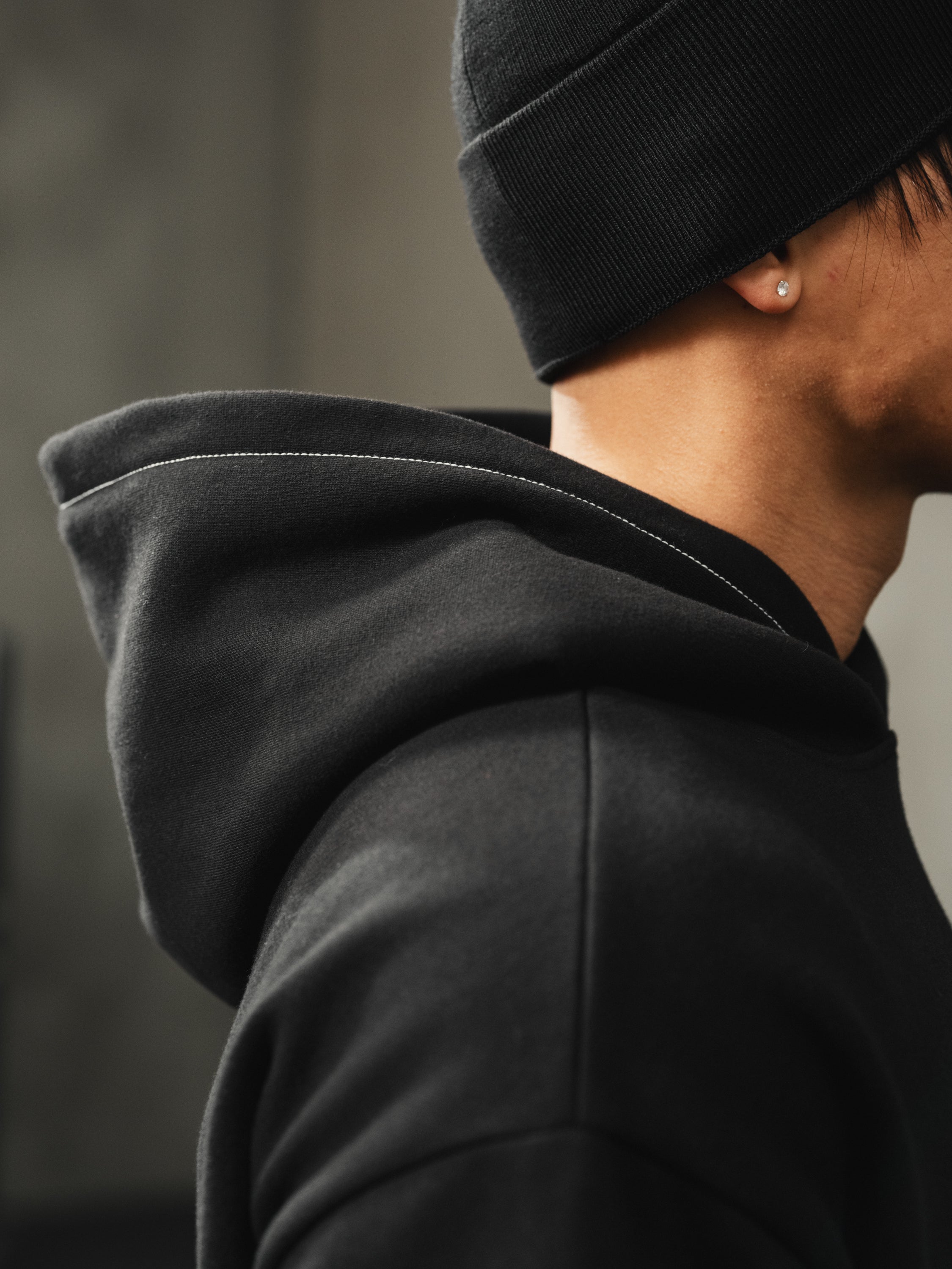 Close-up side view of Ascent Hoodie on model showcasing black hood with contrast white topstitching and relaxed shoulder drape