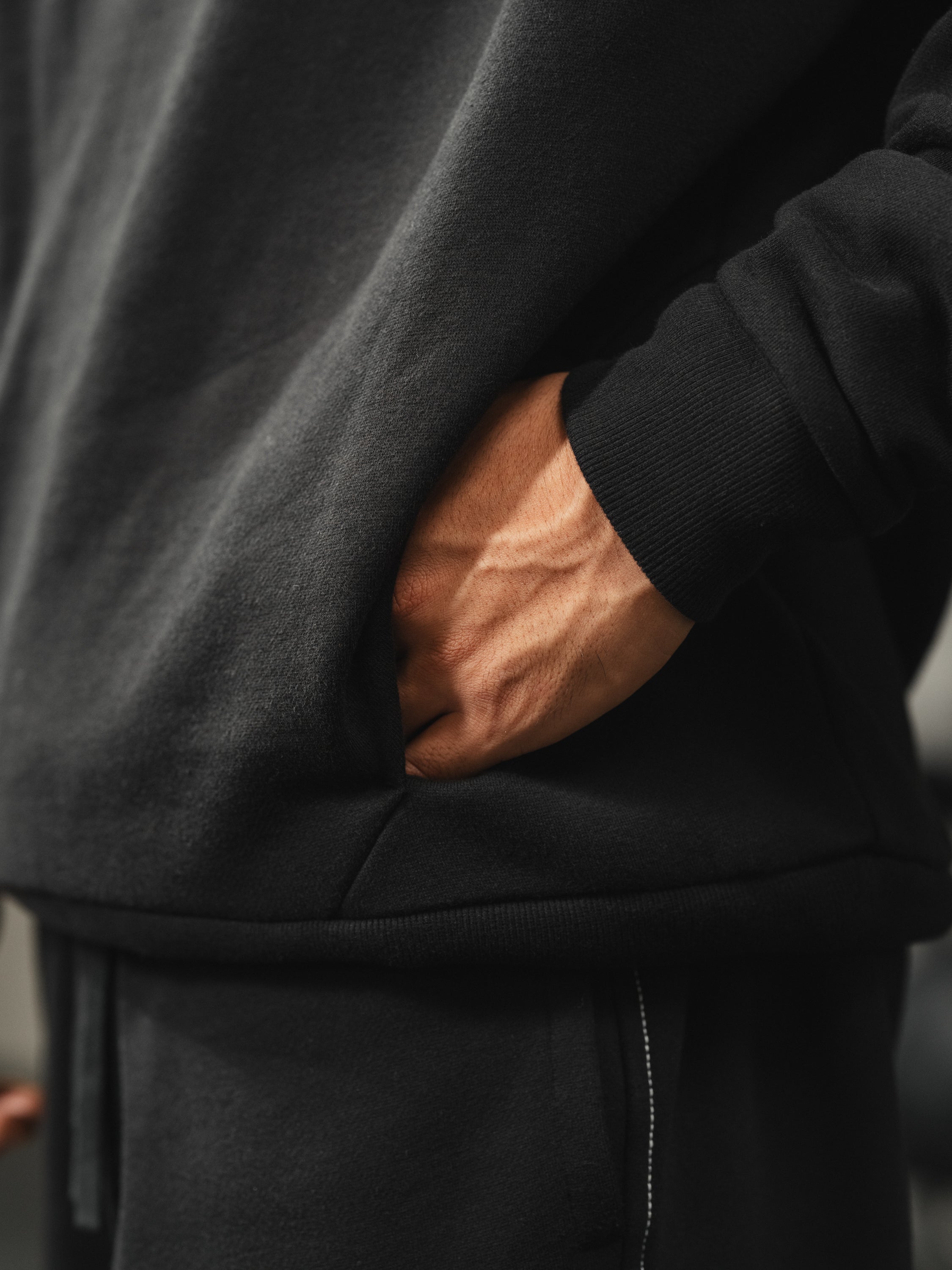 Close-up of Ascent Hoodie showing hand in kangaroo pocket and ribbed cuff on black fabric