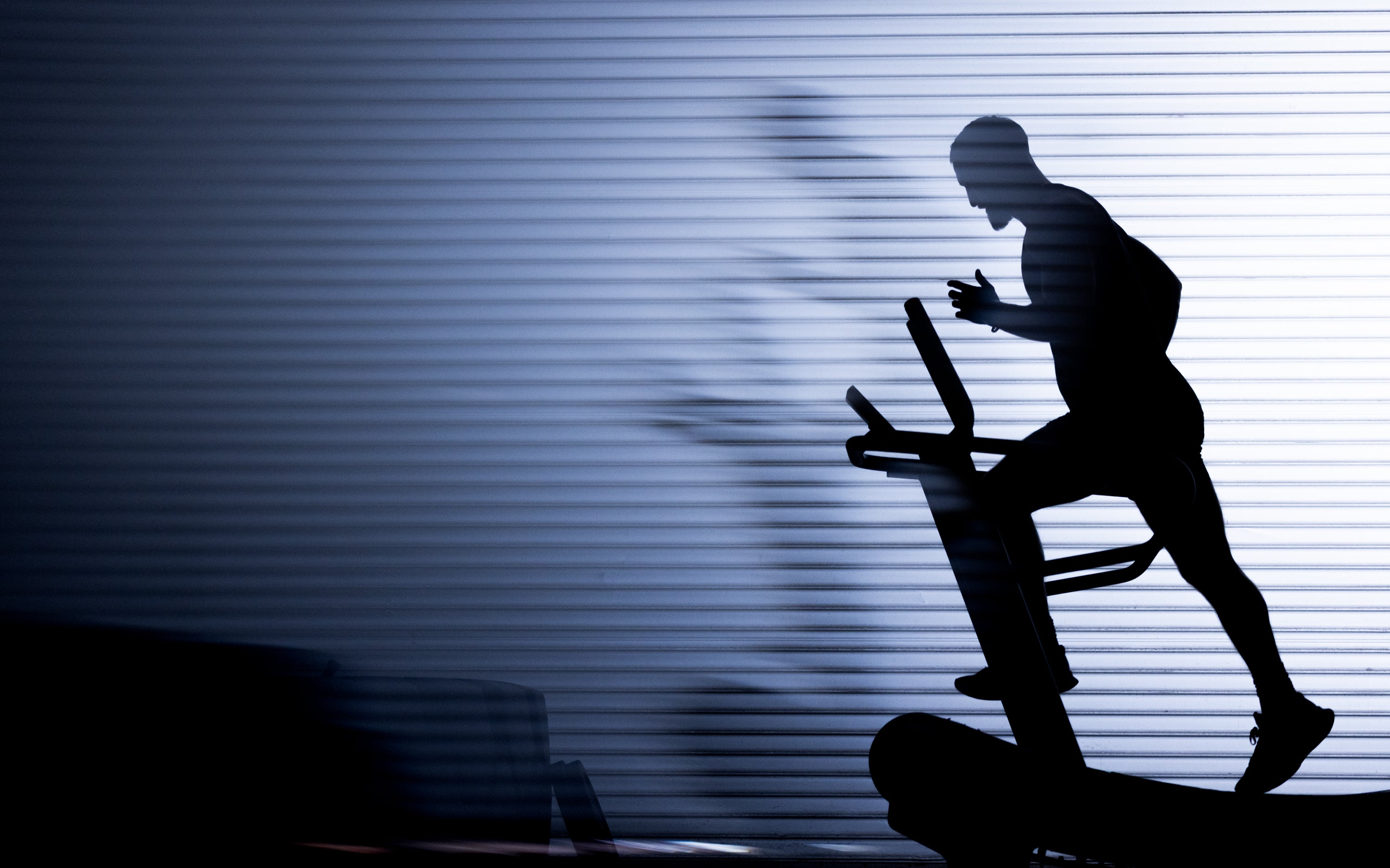 Silhouette of a person cycling on a stationary bike against a striped, backlit wall conveying focused indoor training
