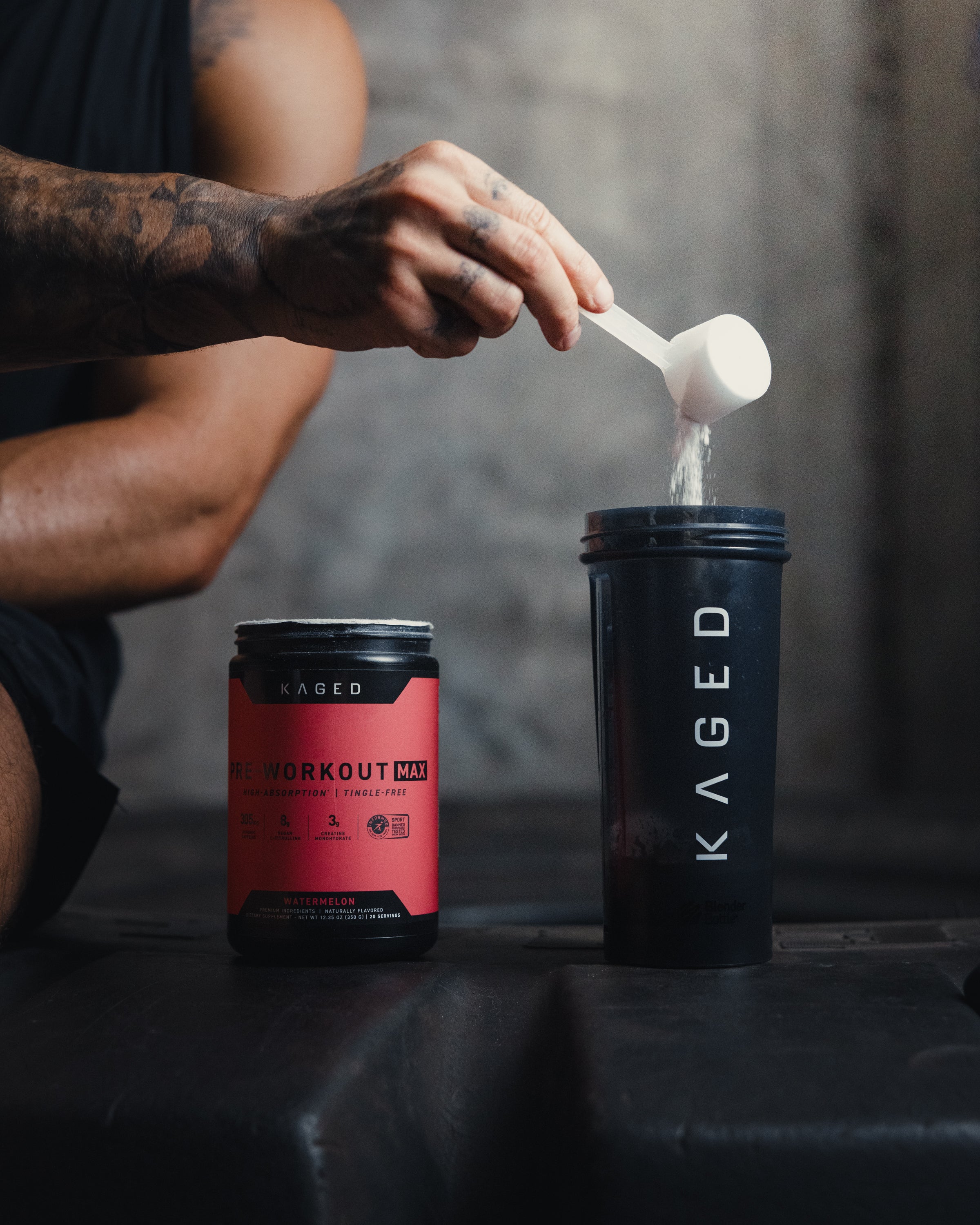 Close-up of Pre-Workout Max tub with scoop pouring powder into a Kaged shaker, watermelon flavor label visible