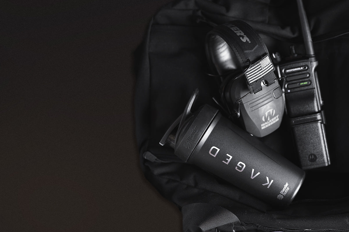 KAGED shaker bottle for hydration resting with tactical headset and two-way radio inside a black backpack
