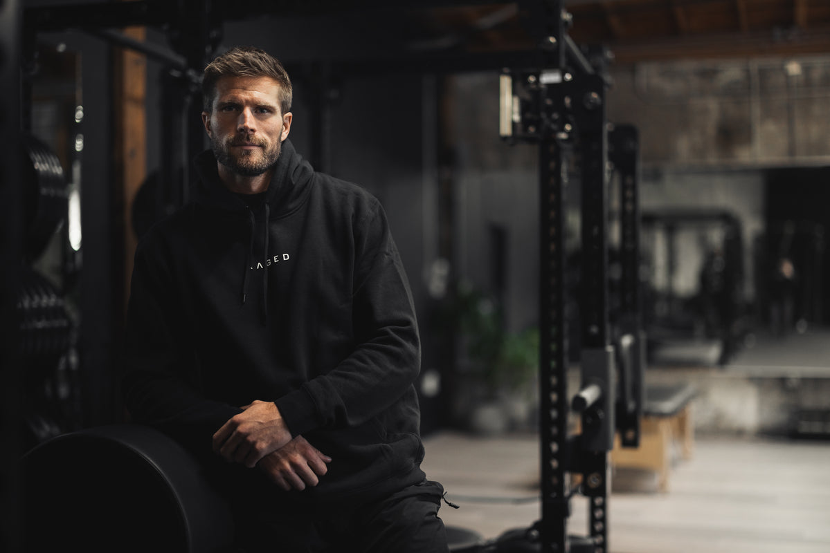 Three-quarter view of Never Stop Evolving hoodie on male model, black pullover with kangaroo pocket and KAGED logo in gym