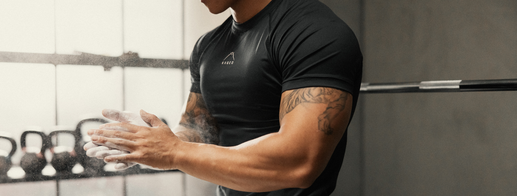 Side-front close-up of Ascent Performance Tee on model showing fitted moisture-wicking fabric and chest KAGED logo in gym