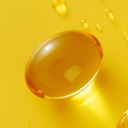 Close-up of amber Vitamin D3 softgel showing translucent gel and reflective highlights on a yellow background